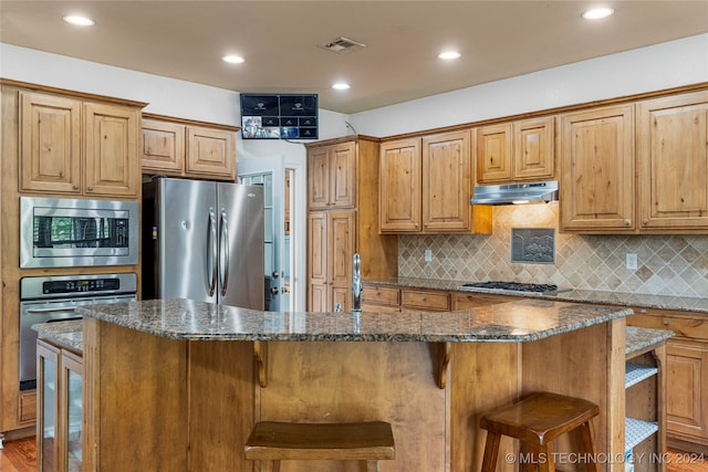 kitchen with a kitchen island, appliances with stainless steel finishes, a breakfast bar, and dark stone countertops