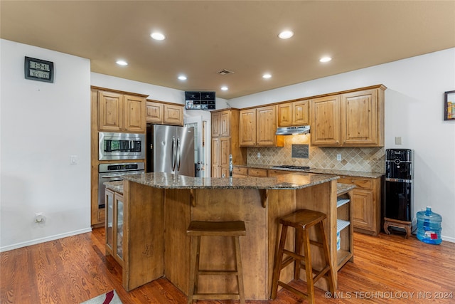 kitchen with a center island, stainless steel appliances, dark stone counters, hardwood / wood-style flooring, and a breakfast bar area