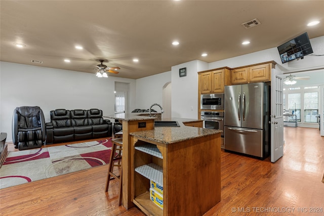 kitchen with dark hardwood / wood-style flooring, stainless steel appliances, dark stone counters, a breakfast bar area, and a center island with sink