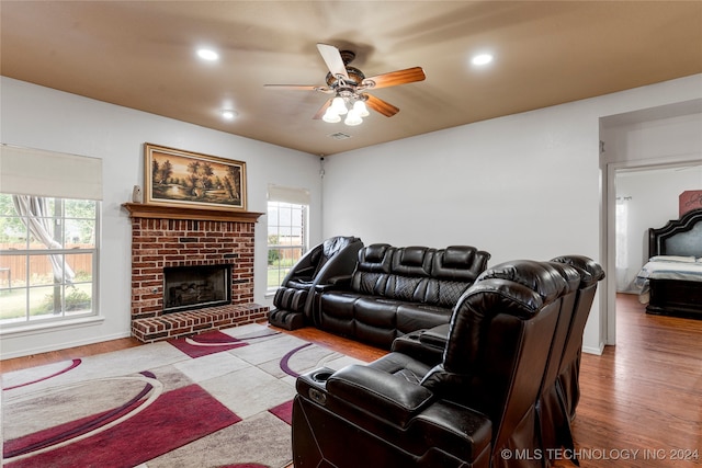 living room featuring light hardwood / wood-style floors, a brick fireplace, a healthy amount of sunlight, and ceiling fan