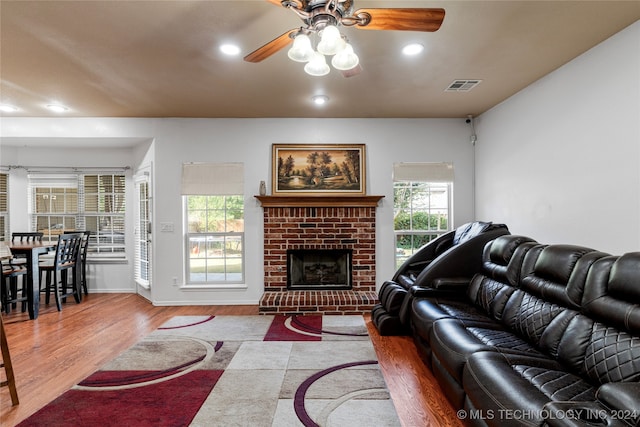 living room featuring light hardwood / wood-style flooring, a brick fireplace, and ceiling fan