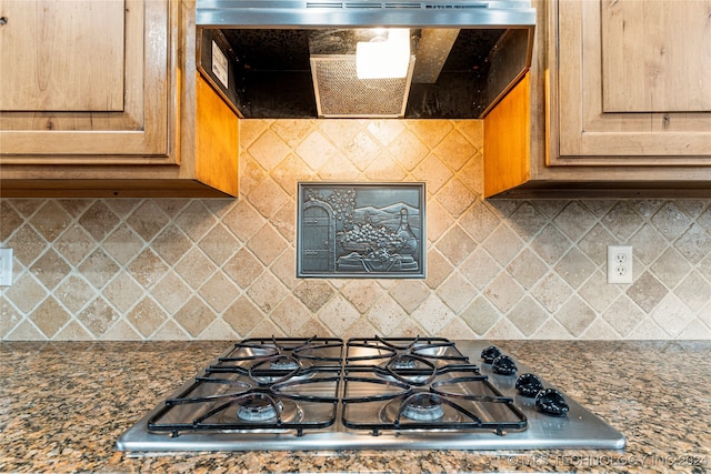 kitchen featuring ventilation hood, decorative backsplash, stainless steel gas stovetop, and dark stone counters