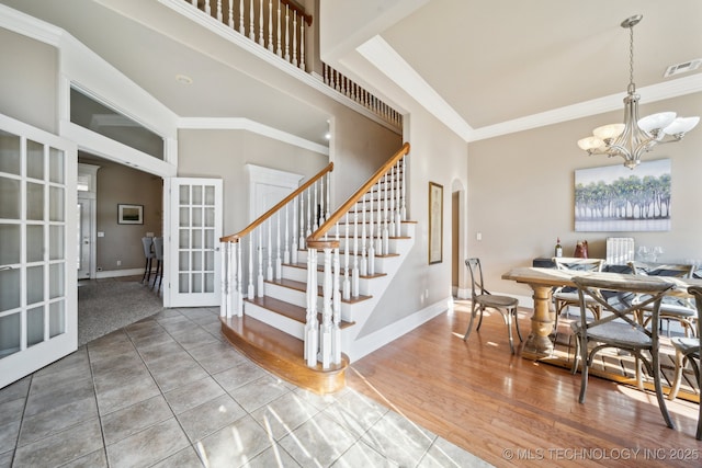 interior space featuring french doors, an inviting chandelier, wood-type flooring, ornamental molding, and a towering ceiling