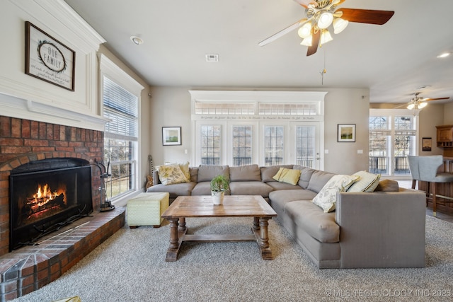 living room with ceiling fan, plenty of natural light, and a brick fireplace