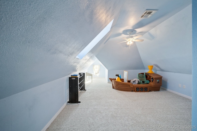 interior space featuring ceiling fan, lofted ceiling with skylight, a textured ceiling, and carpet