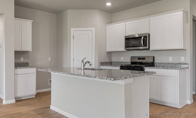 kitchen with appliances with stainless steel finishes, light hardwood / wood-style flooring, white cabinets, and an island with sink