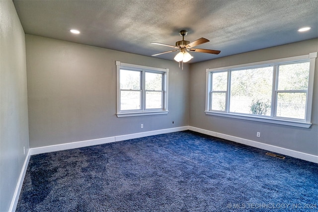 empty room featuring dark colored carpet, a textured ceiling, a healthy amount of sunlight, and ceiling fan