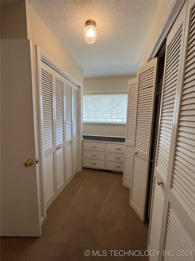 hall with dark colored carpet and a textured ceiling