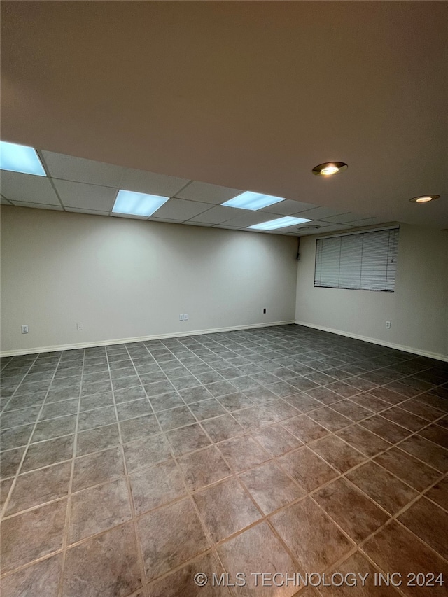 basement featuring dark tile patterned floors and a drop ceiling