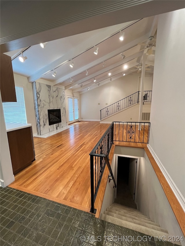 stairway featuring hardwood / wood-style floors, rail lighting, a premium fireplace, ceiling fan, and vaulted ceiling with beams