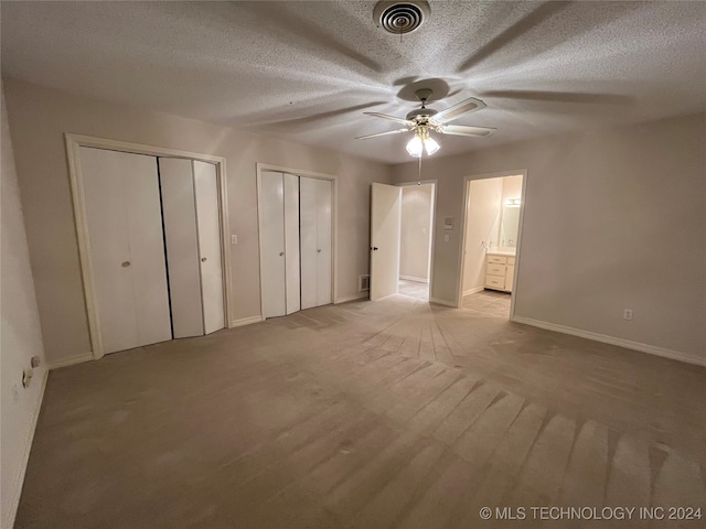 unfurnished bedroom featuring multiple closets, ensuite bath, light colored carpet, a textured ceiling, and ceiling fan