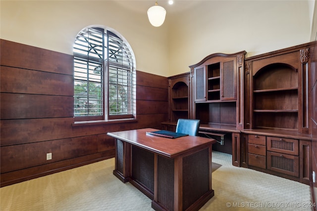 office with light carpet, a towering ceiling, and wood walls