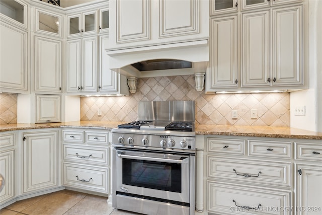 kitchen with light tile patterned floors, backsplash, premium range hood, high end stainless steel range oven, and light stone counters