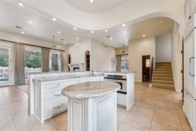 kitchen featuring stainless steel oven, light stone counters, light tile patterned floors, and a kitchen island