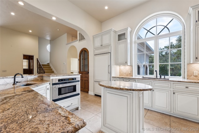 kitchen featuring sink, light stone counters, a kitchen island, and oven