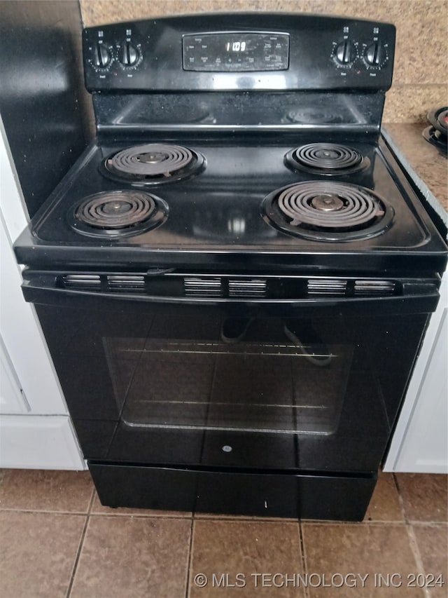 interior details with tile patterned floors, electric range, and white cabinets