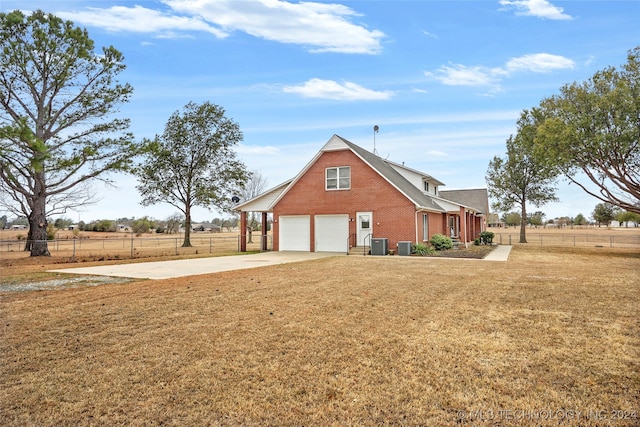 view of side of property with a yard, central air condition unit, a rural view, and a garage