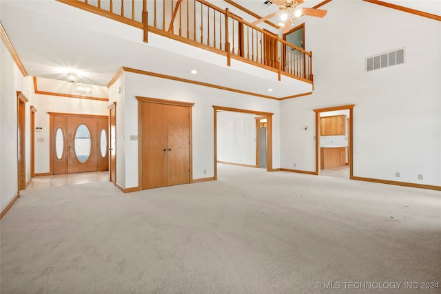 unfurnished living room featuring a towering ceiling, ornamental molding, light carpet, and ceiling fan