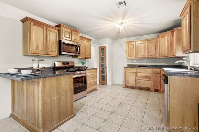 kitchen with kitchen peninsula, light tile patterned floors, appliances with stainless steel finishes, sink, and decorative light fixtures