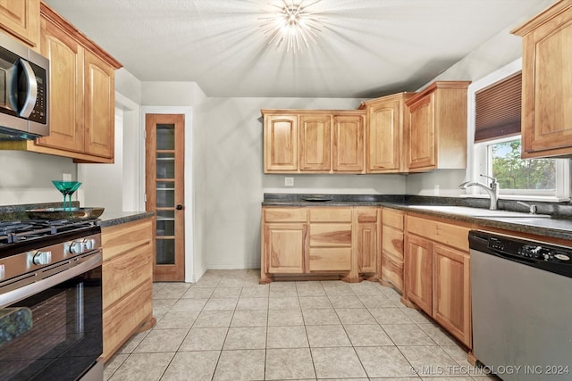 kitchen with appliances with stainless steel finishes, light tile patterned flooring, sink, and dark stone counters