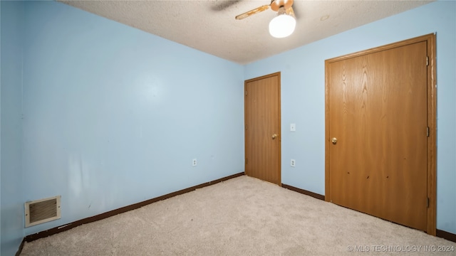 unfurnished bedroom with light carpet, a textured ceiling, and ceiling fan