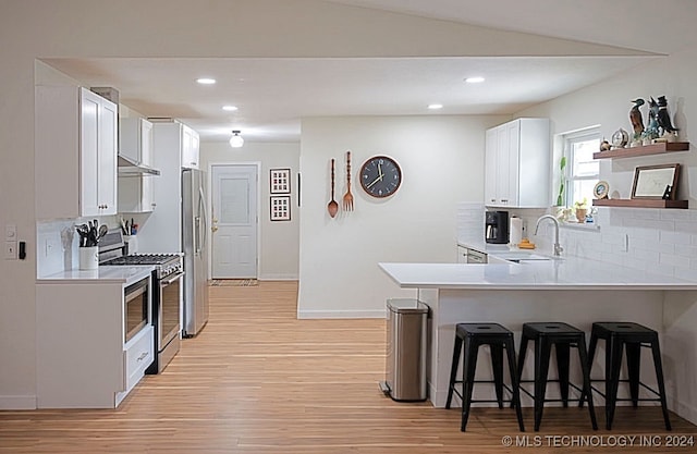 kitchen with white cabinets, kitchen peninsula, a kitchen breakfast bar, light wood-type flooring, and appliances with stainless steel finishes