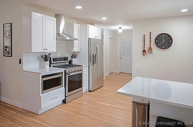 kitchen with tasteful backsplash, stainless steel appliances, wall chimney range hood, light hardwood / wood-style floors, and white cabinets