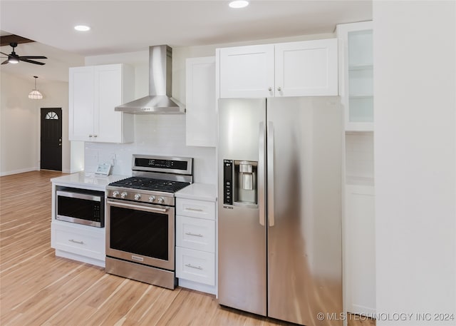 kitchen featuring white cabinets, decorative backsplash, wall chimney exhaust hood, light hardwood / wood-style flooring, and appliances with stainless steel finishes