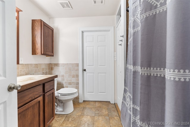 bathroom featuring vanity, toilet, and tile walls