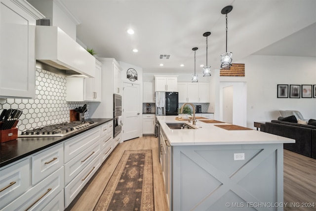 kitchen with light hardwood / wood-style flooring, custom range hood, a center island with sink, white cabinets, and appliances with stainless steel finishes