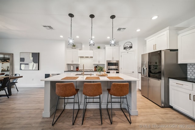 kitchen featuring tasteful backsplash, hanging light fixtures, light hardwood / wood-style floors, stainless steel appliances, and a center island with sink