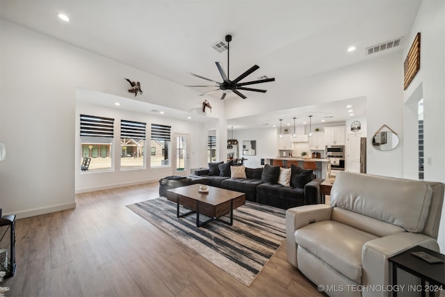 living room featuring a towering ceiling, light wood-type flooring, and ceiling fan