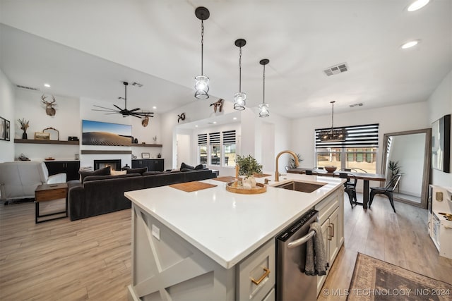 kitchen with hanging light fixtures, a center island with sink, stainless steel dishwasher, light hardwood / wood-style flooring, and sink