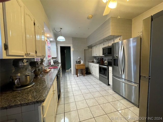 kitchen with dark stone counters, hanging light fixtures, sink, light tile patterned floors, and appliances with stainless steel finishes