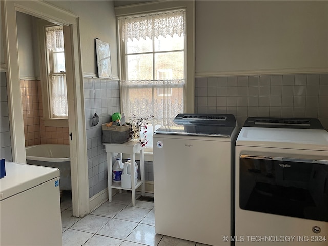 washroom with washing machine and clothes dryer, light tile patterned floors, and tile walls