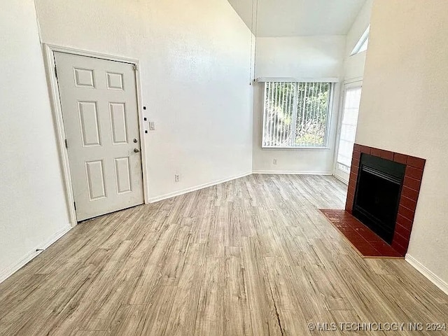 unfurnished living room with a high ceiling, a brick fireplace, and light wood-type flooring