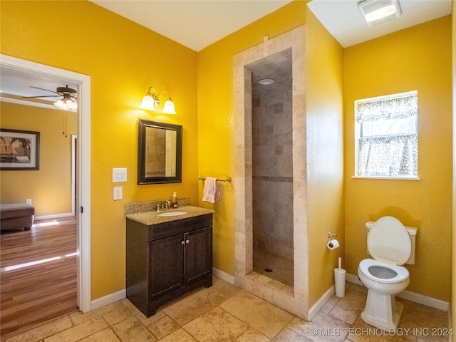 full bathroom featuring toilet, a ceiling fan, vanity, tiled shower, and baseboards