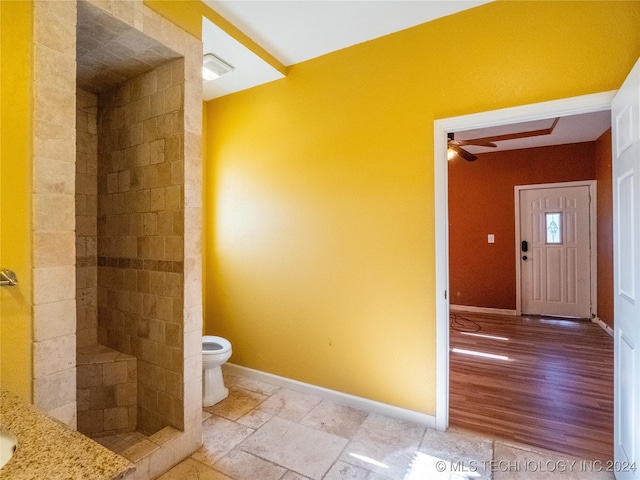 full bathroom featuring baseboards, tiled shower, toilet, ceiling fan, and stone tile flooring