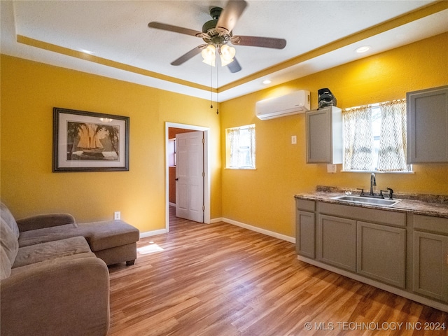 kitchen featuring a raised ceiling, light hardwood / wood-style floors, an AC wall unit, and sink