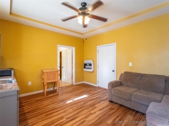 living area with baseboards, light wood-type flooring, a ceiling fan, and heating unit