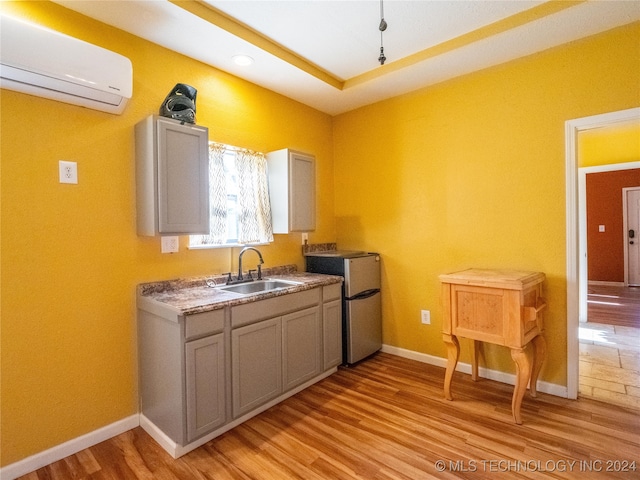 kitchen with baseboards, light wood-style flooring, refrigerator, an AC wall unit, and a sink