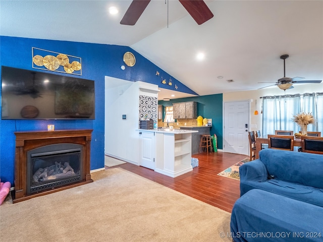 living area featuring lofted ceiling, carpet floors, wood finished floors, a ceiling fan, and a glass covered fireplace