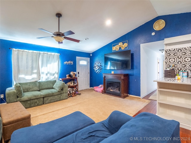 living area featuring vaulted ceiling, ceiling fan, and a glass covered fireplace