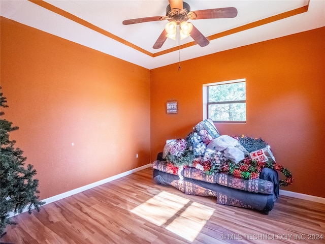 bedroom with hardwood / wood-style floors, ceiling fan, and a raised ceiling