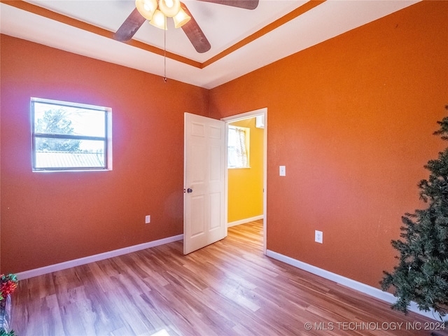 spare room featuring a ceiling fan, a tray ceiling, light wood-style flooring, and baseboards