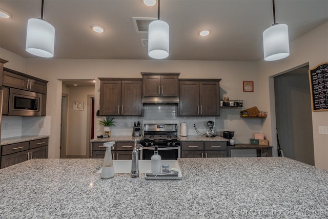 kitchen with appliances with stainless steel finishes, dark brown cabinets, pendant lighting, light stone counters, and decorative backsplash