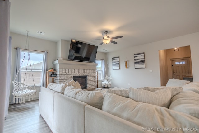 living room featuring a brick fireplace, light wood-type flooring, a healthy amount of sunlight, and ceiling fan