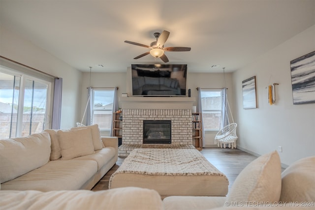 living room featuring hardwood / wood-style floors, a brick fireplace, a healthy amount of sunlight, and ceiling fan