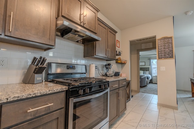 kitchen with backsplash, stainless steel gas range, and light stone counters