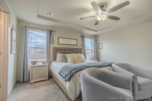 bedroom featuring light colored carpet, a raised ceiling, and ceiling fan